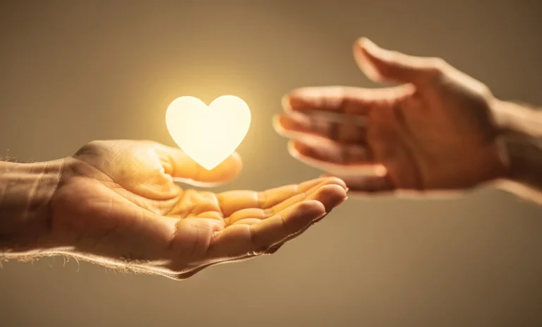 Une main ouverte tend un petit cœur lumineux vers une autre main dans une lumière chaleureuse et apaisante.
